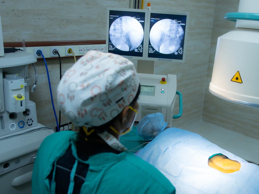 Dr. Kalpana K confirming needle position on twin fluoroscopy monitors during a spine procedure